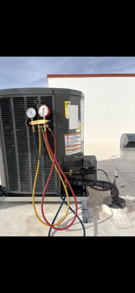 Air Control Services technician with manifold gauges servicing AC unit